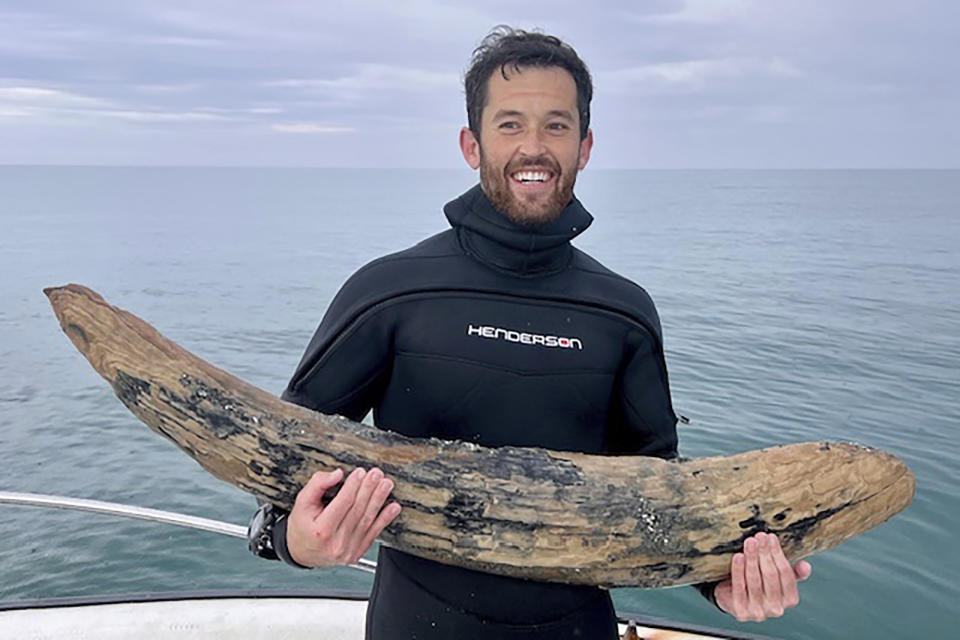 This April 2024 photo taken by Blair Morrow and provided by Alex Lundberg shows Lundberg holding a large section of tusk from a long-extinct mastodon that he and his diver companion found on the sea floor off Florida's Gulf coast. They first thought it was just a large piece of wood. (Blair Morrow via AP)