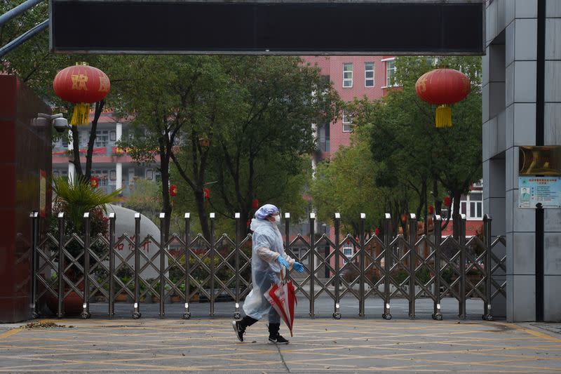 Resident in protective gear walks past the entrance of a closed secondary school in Wuhan, the epicentre of the novel coronavirus outbreak