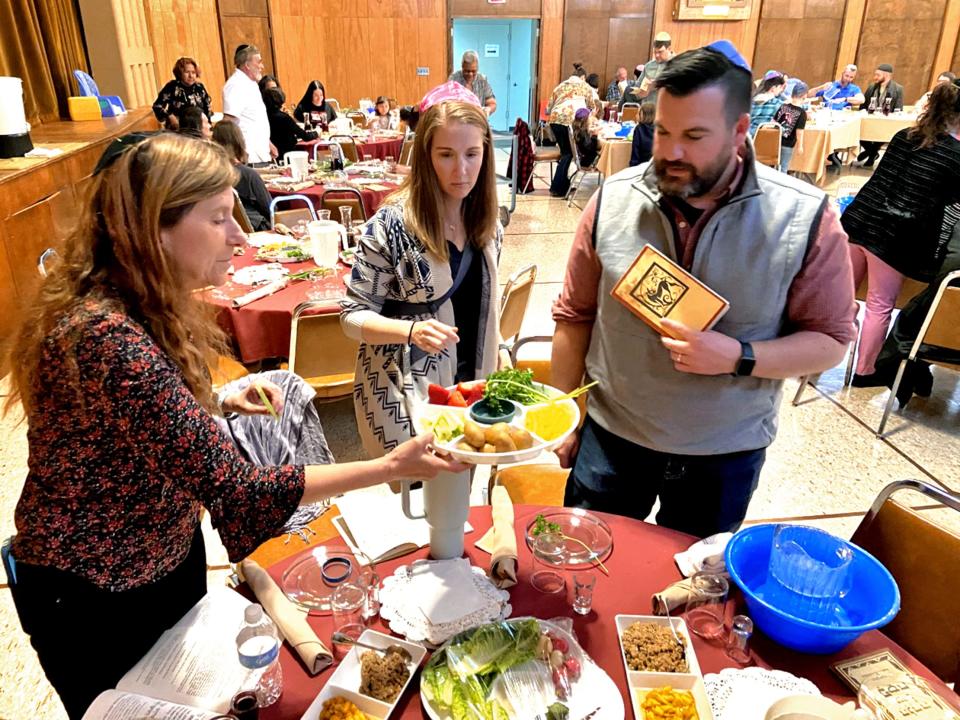 Hali Goss passes a plate of food to Heidi Ross and her husband the Rev. Daniel Ross during a Passover Seder on Wednesday at Emanuel Synagogue in Oklahoma City.