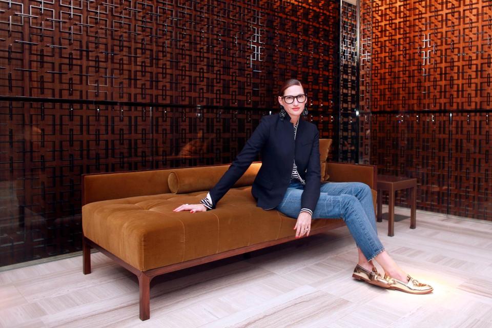 J. Crew's Jenna Lyons sits on brown velvet couch wearing blazer, jeans, and loafers