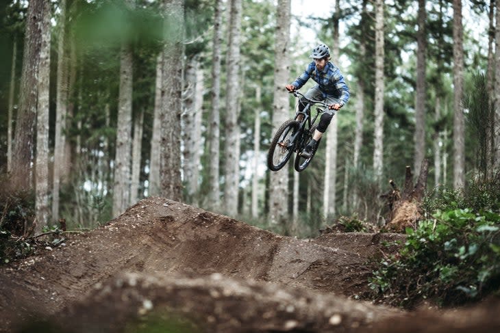 <span class="article__caption">An adult man races down a forest trail, flying through the air from a dirt jump on his mountain bike. Fun and healthy lifestyle image of recreational outdoor activity.</span>