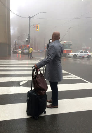 A pedestrian stands at a crosswalk as smoke rises near anintersection in the financial district after reports of a loud blast and heavy smoke could be seen in Toronto, Ontario, Canada May 1, 2017. REUTERS/Anna Mehler Paperny