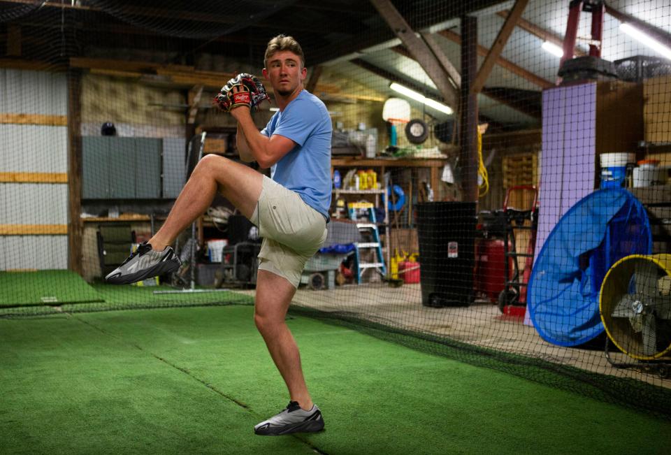 Jacob Miller winds up to throw a pitch in the homemade bull pen and batting cage combo in the garage at his home in Baltimore, Ohio on May 18, 2022. Jacob's father, Jim Miller, built a training area for Jacob to practice in. The training area contains the bull pen and batting cage combo, a weight lifting area, a basketball hoop and some seating with a TV where Jacob can relax with friends.