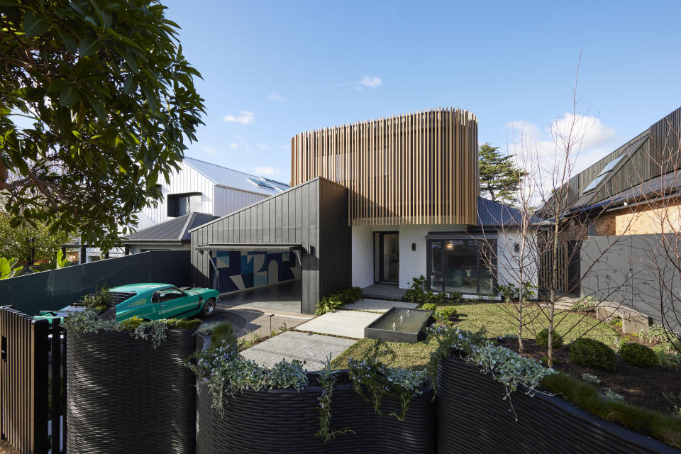 A wide shot of Leah and Ash's front yard with a green car on the left, a grass area on the right and blue sky. 