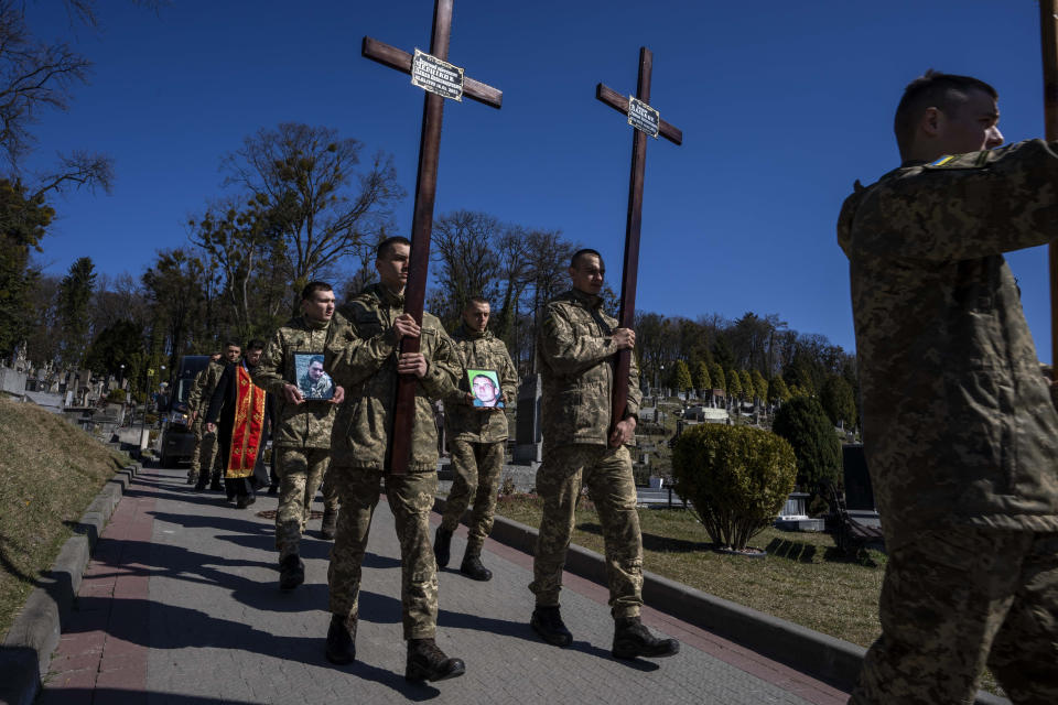 Ukrainian soldiers prepare to bury 32-year-old Senior Lieutenant Pavlo Chernikov, in the photograph at left, and 47-year-old soldier Roman Valkov, during their funeral ceremony, after being killed in action, at the Lychakiv cemetery, in Lviv, western Ukraine, Monday, March 28, 2022. (AP Photo/Nariman El-Mofty)