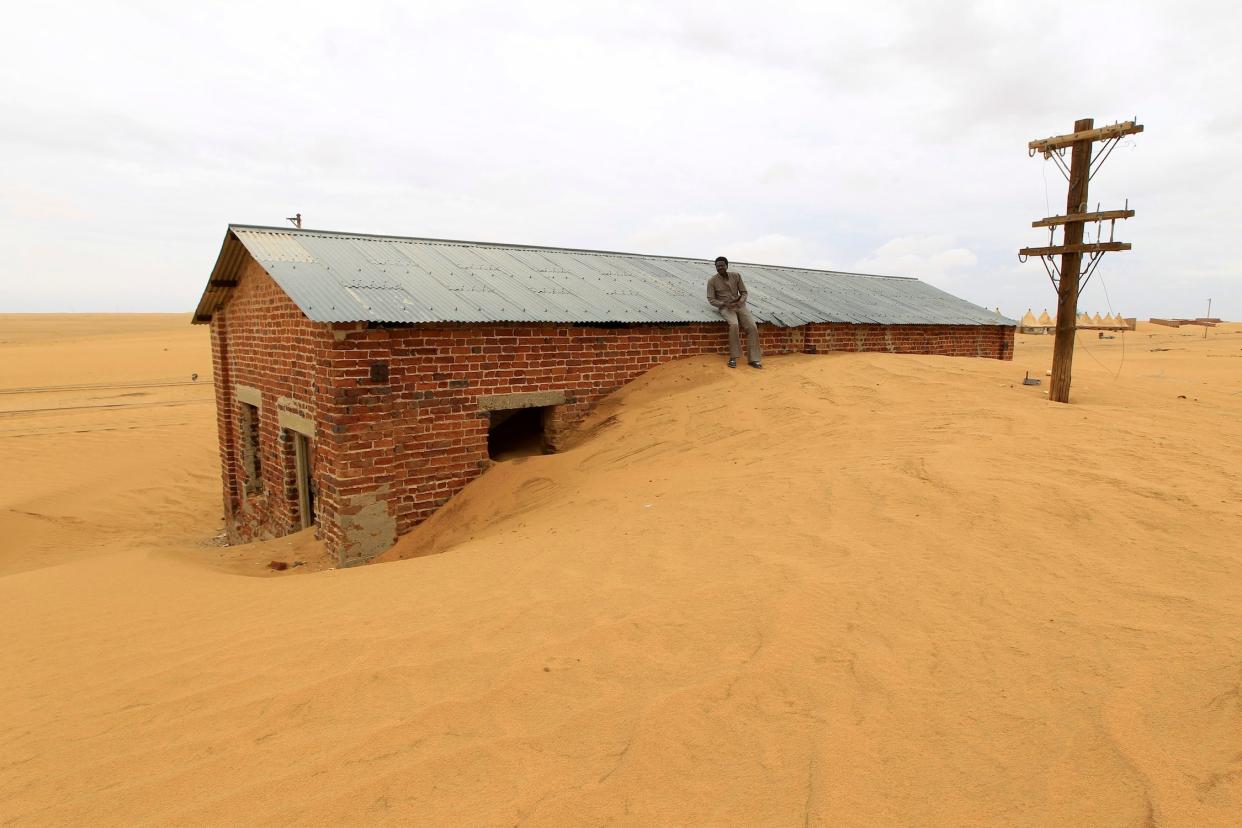 A worker rests on the roof of a building surrounded by sand at Ogrein Railway Station in Sudan