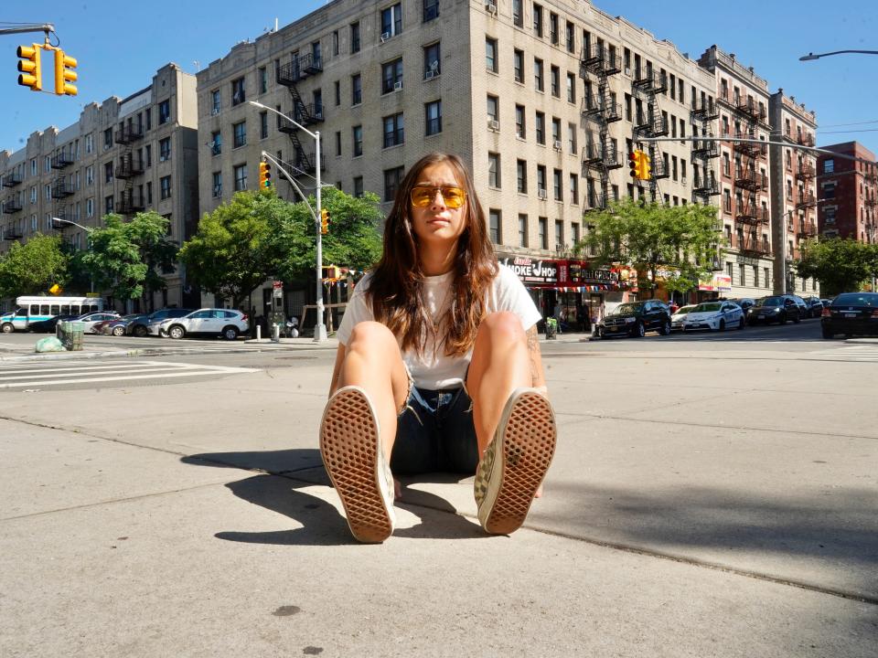 The author sits on the sidewalk with buildings and street lights behind her.