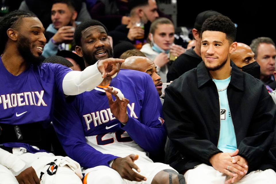 Dec 16, 2021; Phoenix, Arizona, USA; Phoenix Suns forward Jae Crowder (99), center Deandre Ayton (22), and guard Devin Booker (1) watch the action against the Washington Wizards at Footprint Center.