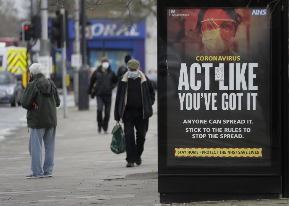 Pedestrians pass a sign on a bus stop in West Ealing in London, Thursday, Feb. 25, 2021. It has been announced that further testing of residents in the London Borough of Ealing will be carried out after additional cases of the coronavirus variant first identified in South Africa were detected. (AP Photo/Kirsty Wigglesworth)