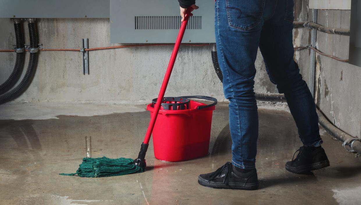 A stock image shows somebody mopping up water in a house damaged by a storm.