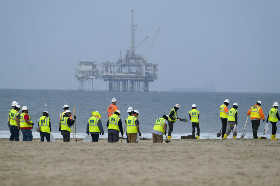FILE - Workers in protective suits continue to clean the contaminated beach with a platform in the background in Huntington Beach, Calif., on Oct. 11, 2021. The owner of an underwater oil pipeline that spilled some 25,000 gallons of crude into the ocean off Southern California will pay nearly $1 million in cleanup costs. The Orange County Board of Supervisors on Tuesday, July 26, 2022 agreed to accept a proposed claim settlement with Amplify Energy Corp. over the costs of dealing with last October’s spill off Huntington Beach. (AP Photo/Ringo H.W. Chiu, File)
