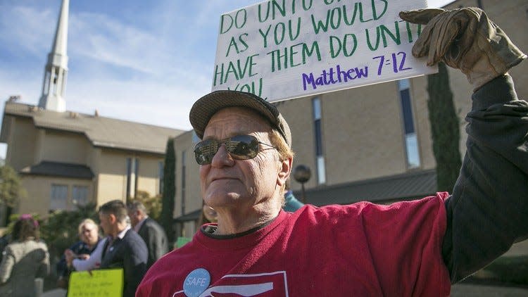 A protester stands in front of a sign bearing the Scripture Matthew 7:12, also known as "the Golden Rule."