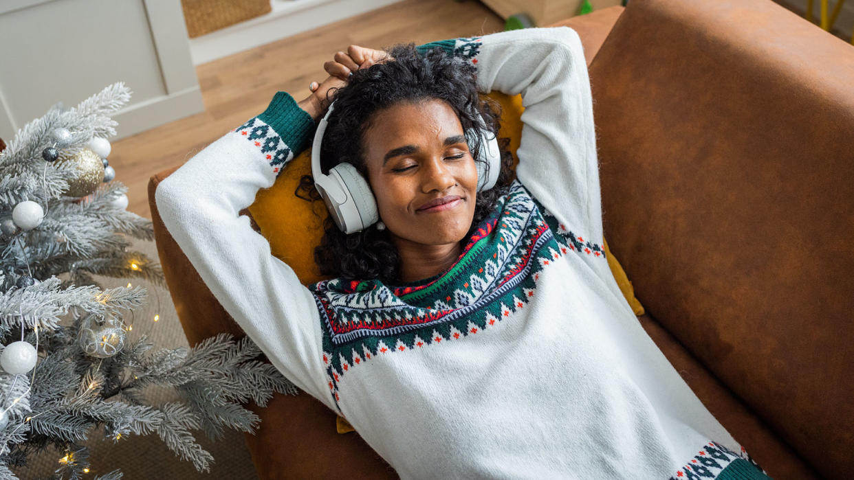  Girl listening to Christmas songs on headphones, relaxing next to the tree. 