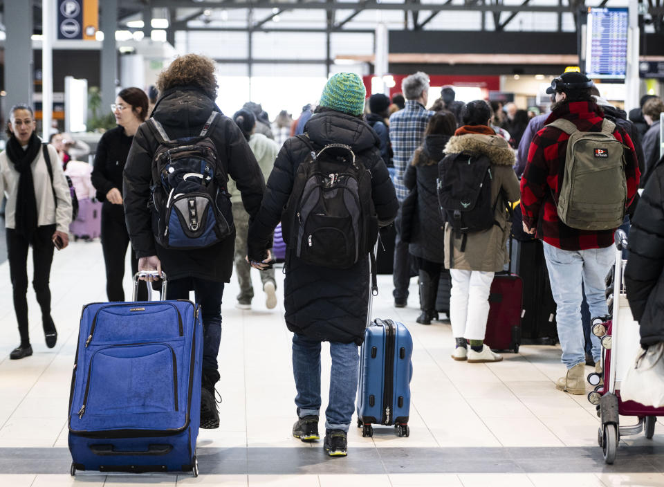 Travellers hold hands as they pass others lining up at the Ottawa International Airport, as airlines cancel or delay flights during a major storm in Ottawa, on Friday, Dec. 23, 2022. (Justin Tang /The Canadian Press via AP)