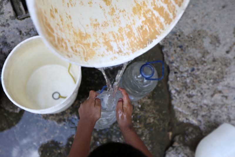 A child helps a man to fill plastic containers with water from an unknown source in the low-income neighbourhood of Petare amid the coronavirus disease (COVID-19) outbreak in Caracas