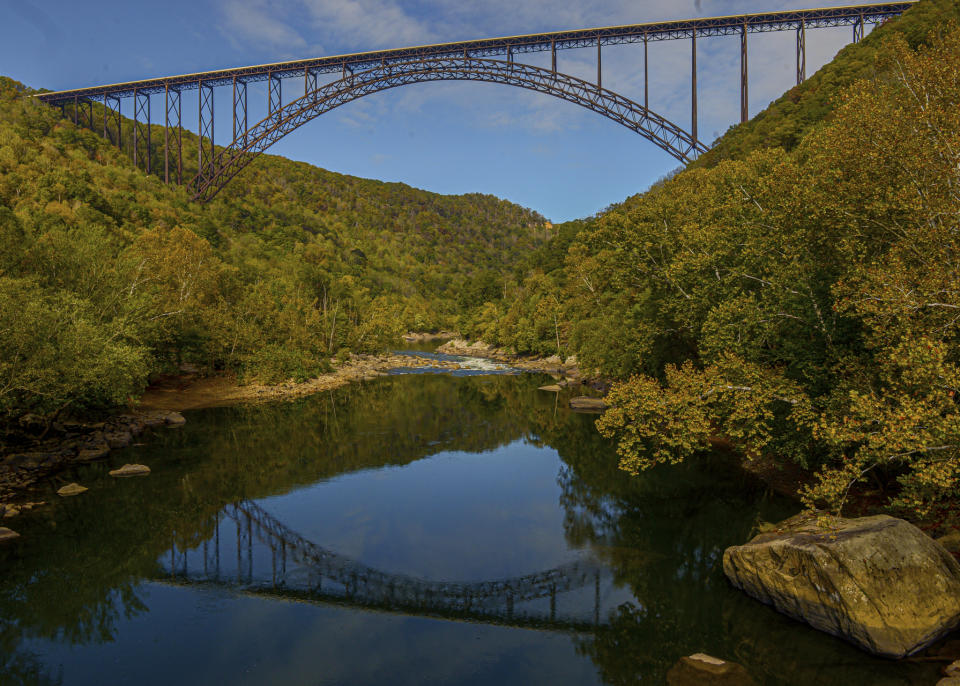 FILE - The New River Gorge Bridge is reflected in the water as seen from Fayette Station, Oct. 9, 2019, in Fayetteville, W.Va. A program offering cash and free outdoor adventures to remote workers to move to West Virginia with the hope of offsetting population losses has added the New River Gorge region where out-of-state workers can apply to live. The public-private program Ascend West Virginia said Tuesday, June 20, 2023, that applications are being accepted for the scenic region. (F. Brian Ferguson/Charleston Gazette-Mail via AP, File)