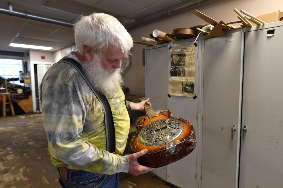 Paul Williams inspects the damage to a dobro guitar damaged by floodwaters from Troublesome Creek at the Applachian School of Luthery workshop and museum in Hindman, Ky., Sunday, July 31, 2022. (AP Photo/Timothy D. Easley)