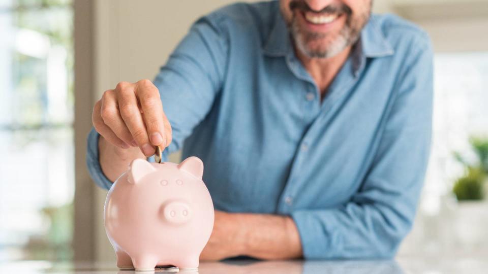 Un homme souriant met de l'argent dans une tirelire