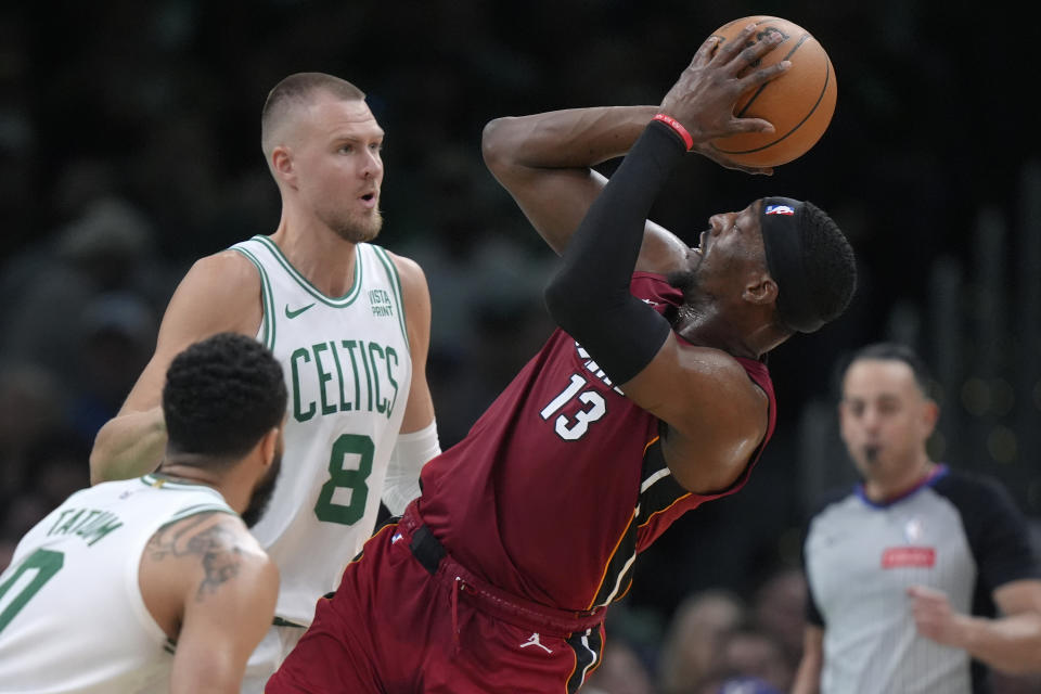 Miami Heat center Bam Adebayo (13) looks to shoot at the basket as Boston Celtics center Kristaps Porzingis (8) and forward Jayson Tatum (0) defend in the first half of Game 1 of an NBA basketball first-round playoff series, Sunday, April 21, 2024, in Boston. (AP Photo/Steven Senne)