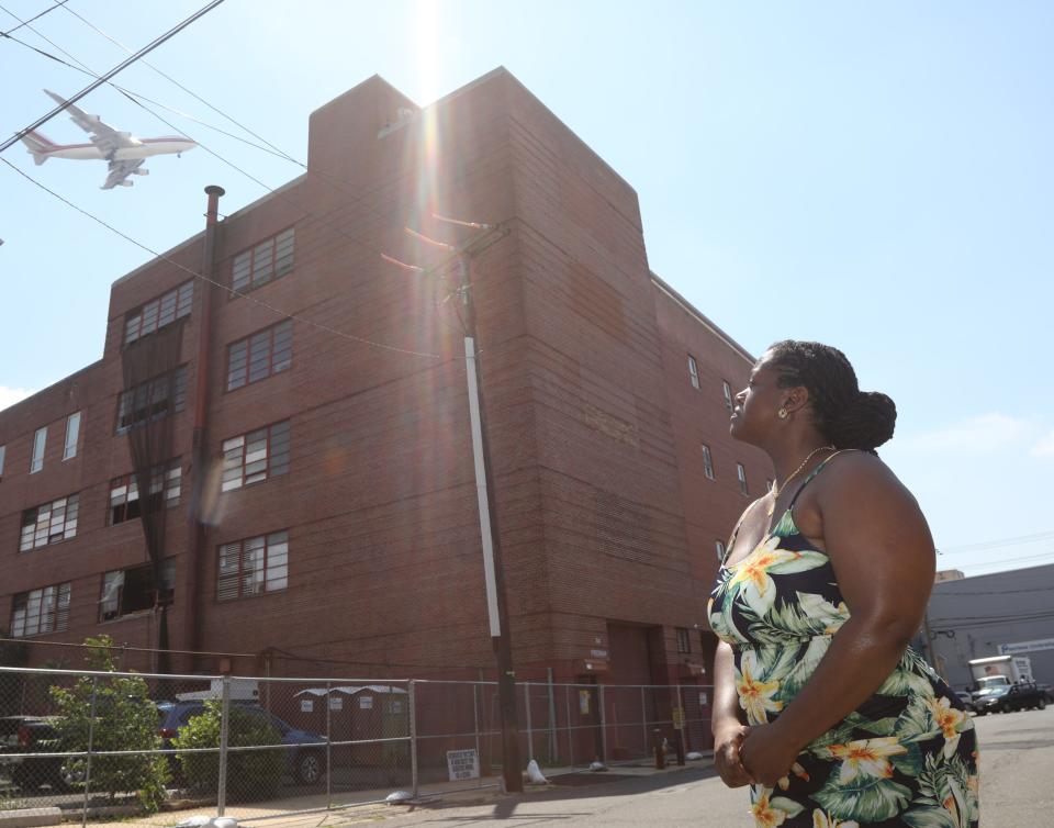 Tanisha Garner stands in front of a former beer plant while a plane passes overhead. The building is among the many structures that trap heat and contribute to high temperatures for residents of Newark's Ironbound section.  July 1, 2022.