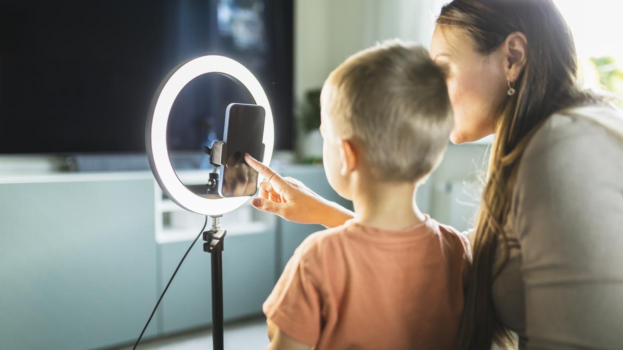  Mother live streaming with son on smart phone with ring light at home. 