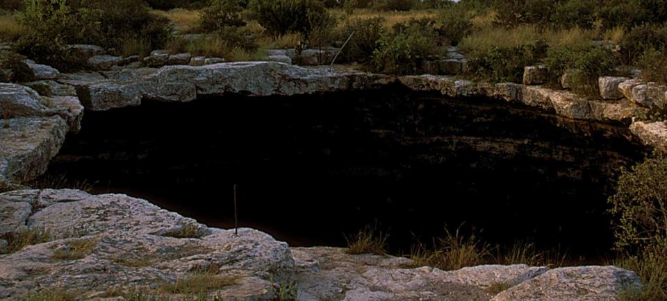 a large dark sinkhole surrounded by rocks