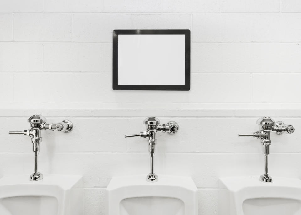 Three urinals in a row on a wall below a blank framed screen