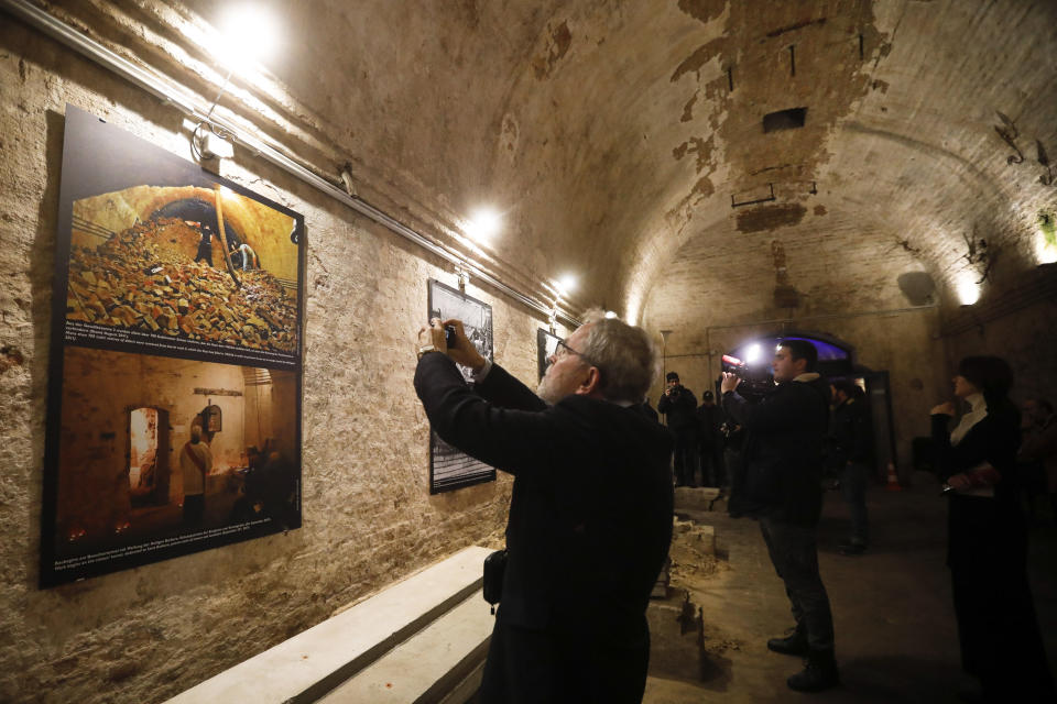 Personas observan fotografías históricas mientras esperan ver un túnel de escape bajo el Muro de Berlín, que dividió la ciudad durante 28 años durante la Guerra Fría, es iluminado ya que se abrió al público por primera vez en la historia el jueves 7 de noviembre de 2019 en Berlín, Alemania. (AP Foto/Markus Schreiber)