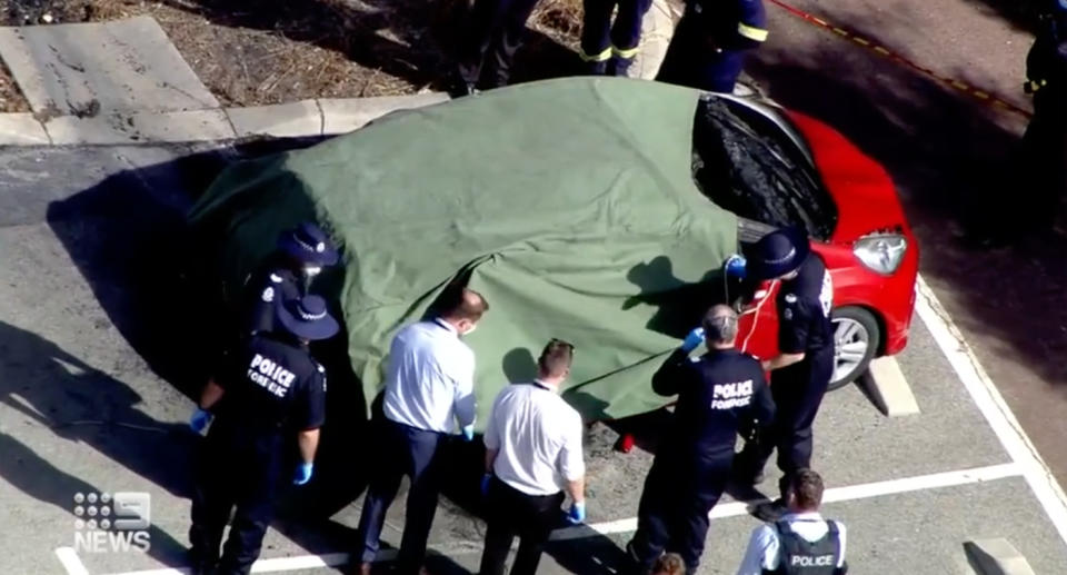 Firefighters and police looking at the family's burnt out car. 