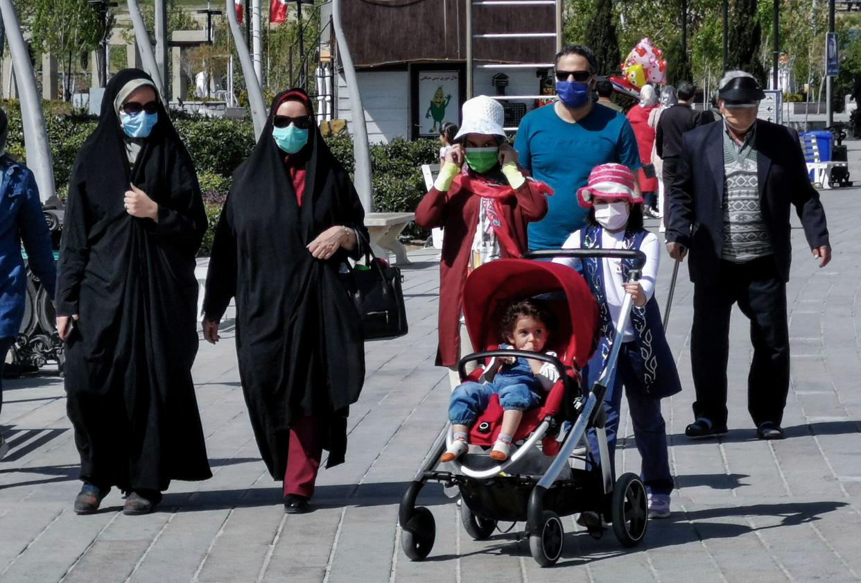 People wearing protective masks amid the coronavirus pandemic walk near the shore of Chitgar Lake in Iran's capital Tehran, on April 5, 2021.