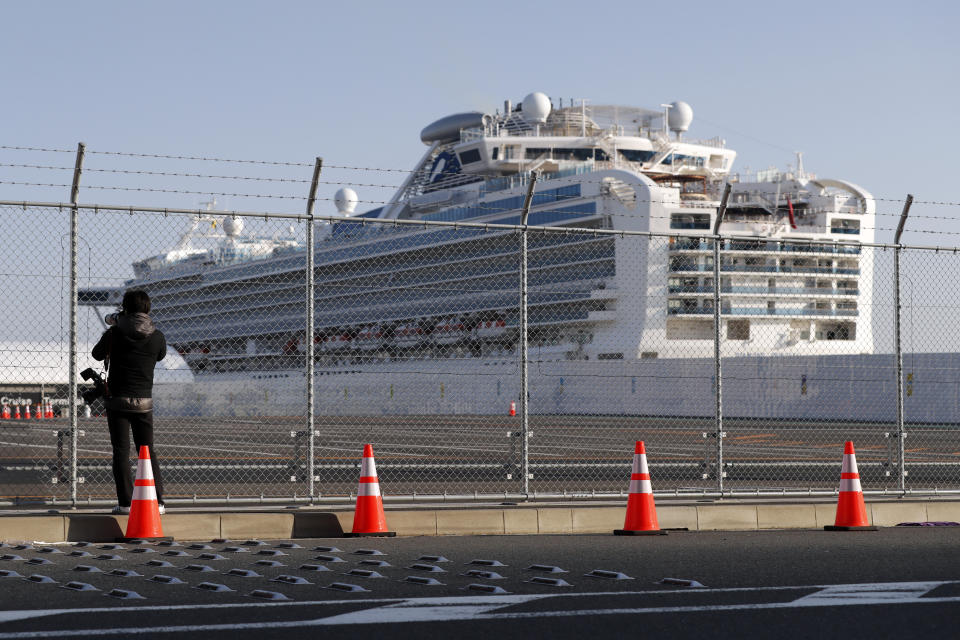 A photographer takes photos near the quarantined Diamond Princess cruise ship anchored at a port in Yokohama, near Tokyo, Friday, Feb. 21, 2020. Passengers tested negative for COVID-19 started disembarking since Wednesday. (AP Photo/Eugene Hoshiko)