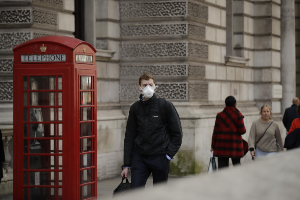 A man wearing a face mask walks past a traditional British red phone box near Parliament Square in central London, Wednesday, March 11, 2020. A British government minister Nadine Dorries, who is a junior Heath minster has tested positive for the coronavirus and is self isolating. For most people, the new coronavirus causes only mild or moderate symptoms, such as fever and cough. For some, especially older adults and people with existing health problems, it can cause more severe illness, including pneumonia. (AP Photo/Matt Dunham)