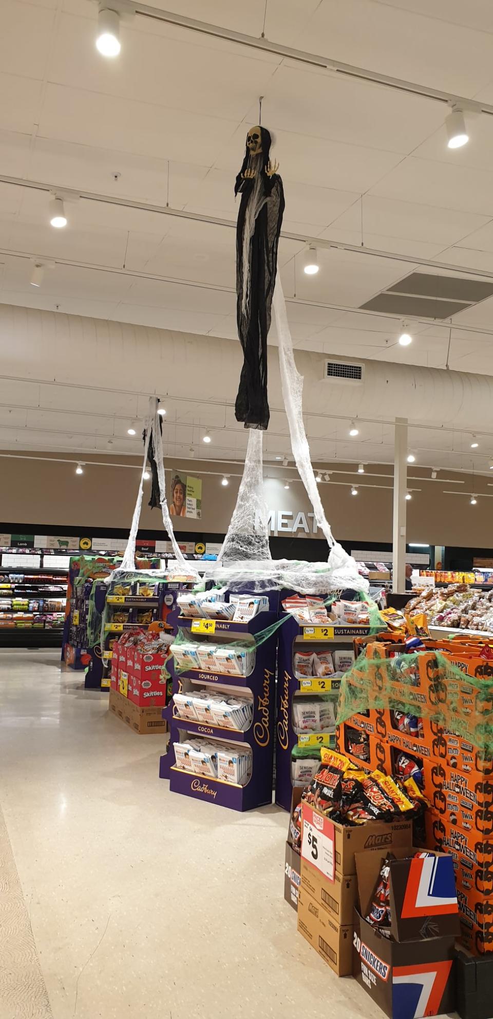 Woolworths in store display showing chocolate, cobwebs, and a cloaked skeleton hanging prop. Source: Facebook