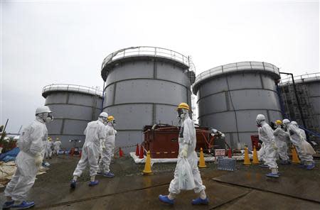 Members of the media and Tokyo Electric Power Co. (TEPCO) employees wearing protective suits and masks walk past storage tanks for radioactive water in the H4 area at the tsunami-crippled TEPCO Fukushima Daiichi nuclear power plant in Fukushima prefecture, in this file picture taken November 7, 2013. REUTERS/Tomohiro Ohsumi