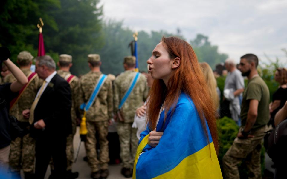 A woman wrapped in a Ukrainian flag attends the funeral of activist and soldier Roman Ratushnyi - Natacha Pisarenko/AP Photo