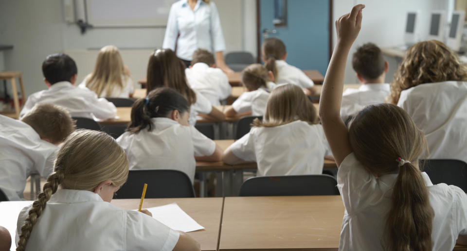 Girl (8-10) raising hand in classroom, rear view. Source: Getty Images 