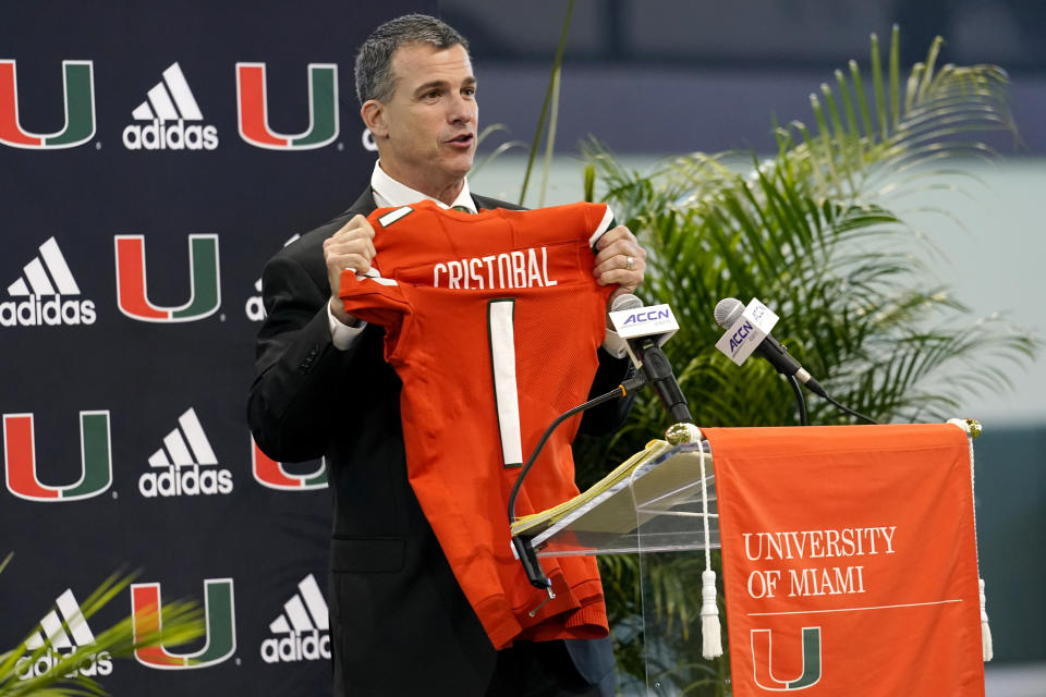 Miami new football coach, Mario Cristobal, holds up a jersey after being introduced at a news conference Tuesday, Dec. 7, 2021, in Coral Gables, Fla. Cristobal is returning to his alma mater, where he won two championships as a player. (AP Photo/Lynne Sladky)