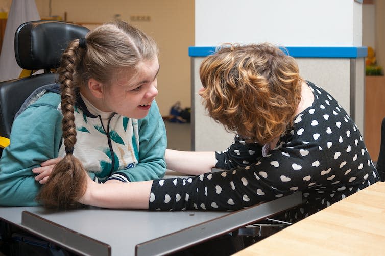 A girl in plaits looks at a woman in a blue and white top.