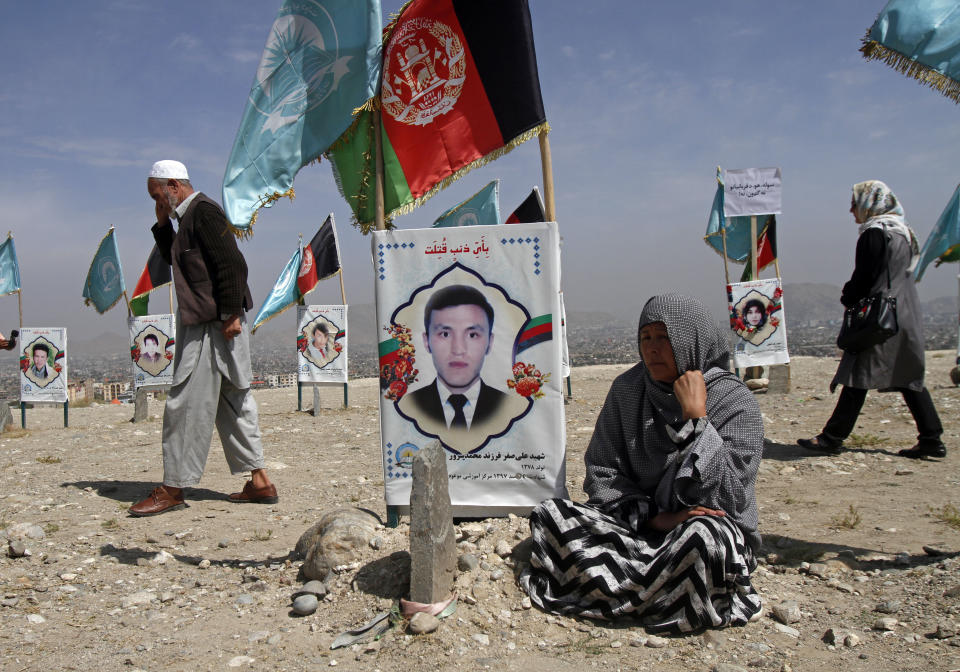 An Afghan woman sits next to the grave of her son, adorned with his picture, on the outskirts of Kabul, Afghanistan, Monday, Sept 14, 2020. Scores of friends and families of students who were killed in local conflicts are gathering in a cemetery to call for a permanent countrywide ceasefire from the parties to the intra-Afghan peace conference taking place in Doha, Qatar. (AP Photo/Rahmat Gul)