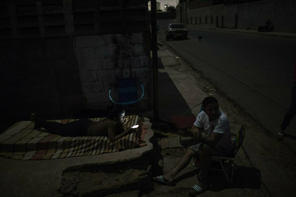 In this May 15, 2019 photo, Marjorie Marcano uses her cell phone while preparing to sleep on a mattress on the sidewalk outside her home, due to a black out in Maracaibo, Venezuela. " I am leaving for Peru tomorrow, I am tired of these endless black outs, its impossible to live in these conditions", Marjorie said. (AP Photo/Rodrigo Abd)