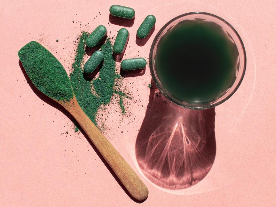 Glass with chlorella drink, spirulina and chlorella powder and tablets on a pink background