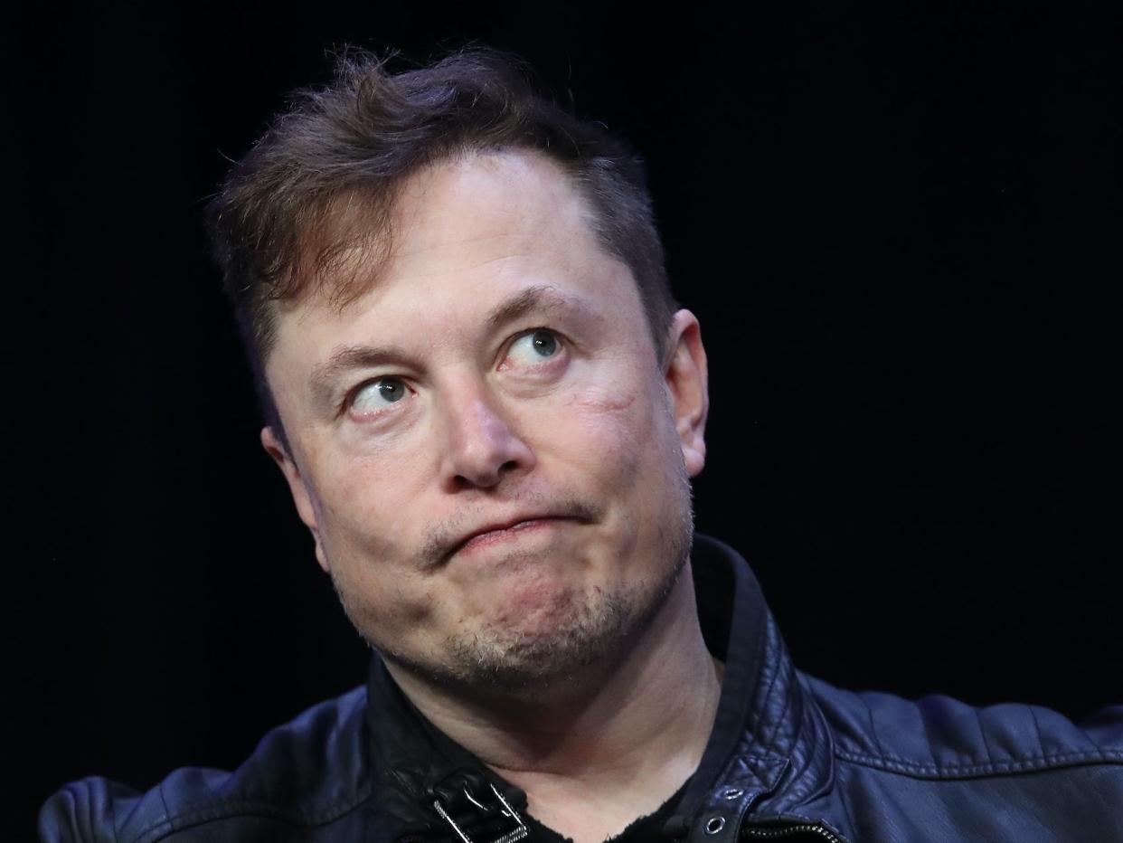 Elon Musk grimaces while looking off to side against black backdrop