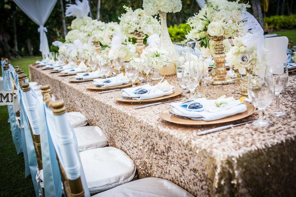 A wedding table set with a gold sparkly tablecloth and blue ribbons on chairs