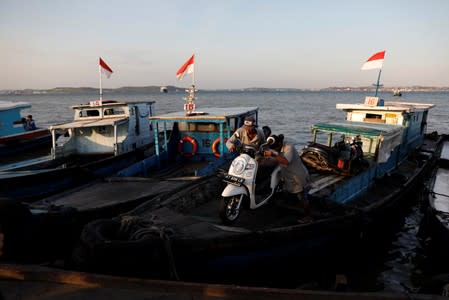 People unload a motorbike from a wooden boat as they arrive from Balikpapan at a port in North Penajam Paser regency, East Kalimantan province