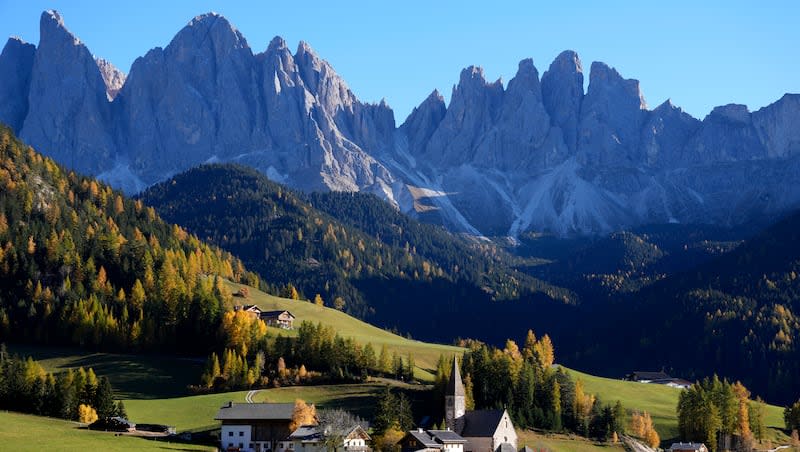 Colorful trees stand around a church at the Dolomites mountains in St. Maddalena, St. Magdalena, in Val di Funes (Villnoess) as the sun sets, in northern Italian province of South Tyrol, Italy, Thursday, Oct. 28, 2021.