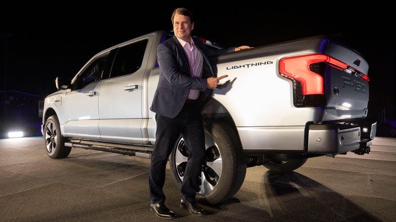 Ford CEO Jim Farley poses with an F-150 Lighting, gesturing to its logo near the tailgate.