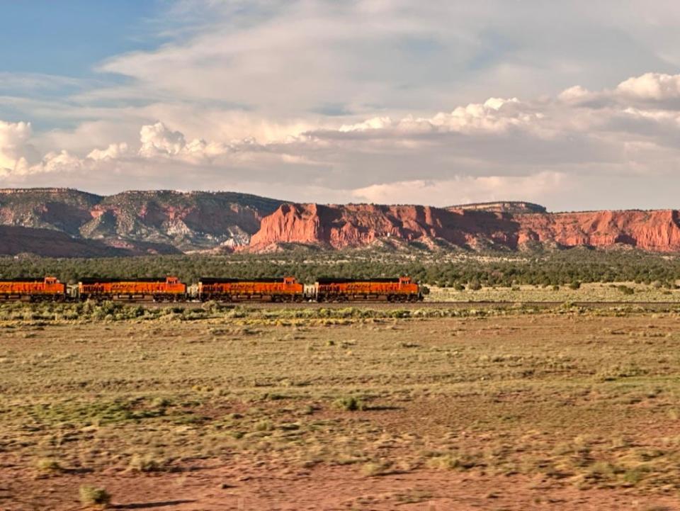 A train passing through New Mexico, with green plains and red rock mountains.