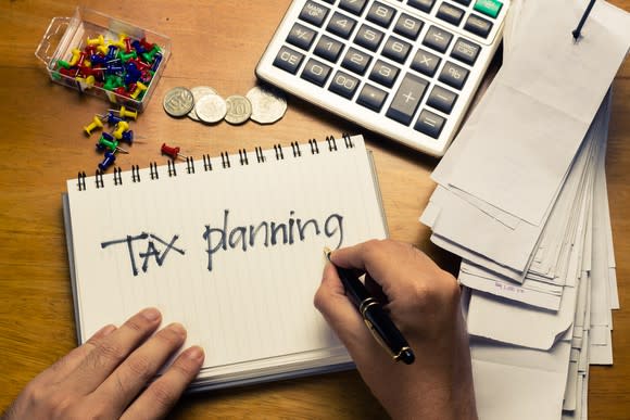 Hands writing tax planning on a notebook, next to a calculator and stack of receipts.