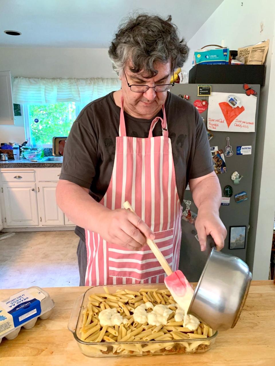 Greek dad putting bechamel sauce over pasta for pastitio