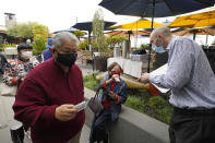 FILE - In this Aug. 20, 2021, file photo, host Jason Pryor, right, checks the vaccination and identification cards of diners as they enter the Waterbar restaurant in San Francisco. Ticket agents dutifully ascertain the vaccination status of everyone passing through the turnstile at pro sports venues in some cities from Seattle and New York, and restaurant hosts do the same in many places. (AP Photo/Eric Risberg, File)